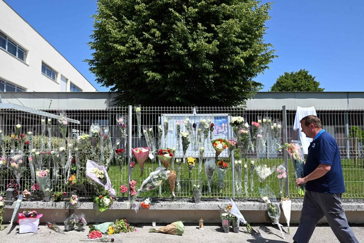 A man walks past flowers on the fence of Francoise Dolto middle school in Nogent on June 11, 2025, a day after a secondary school pupil was arrested after killing a 31-year-old school assistant with a knife during a bag search. (Photo by FRANCOIS NASCIMBENI / AFP)
